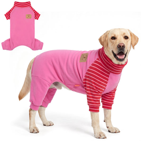 Tan dog wearing pink onesie pajamas with red striped sleeves beside a flat lay