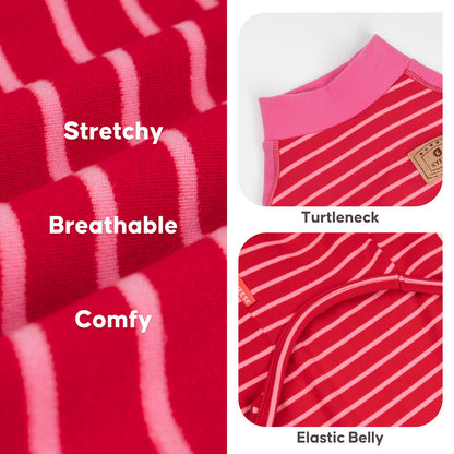 Cream French bulldog standing on a sofa in red striped pajamas with pink sleeves