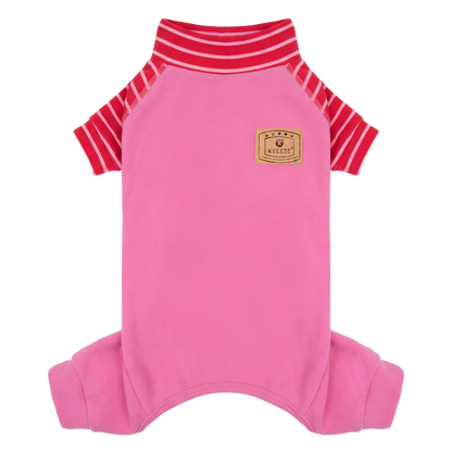 Small tan dog seated outdoors wearing pink pajamas with red striped sleeves