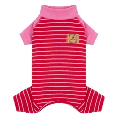 Small tan dog sitting outdoors in red striped onesie pajamas with pink sleeves